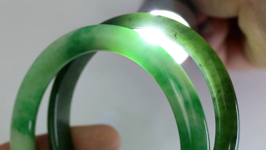 One nephrite jade bangle and one jadeite jade bangle with a penlight shining through the material, showcasing the apparent difference between the two gemstones