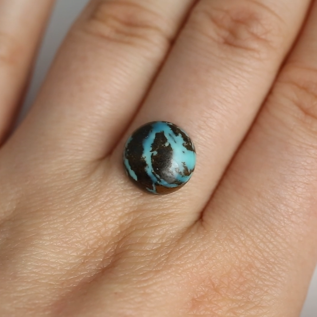 Close-up of a hand wearing a ring with a blue stone on a plain background