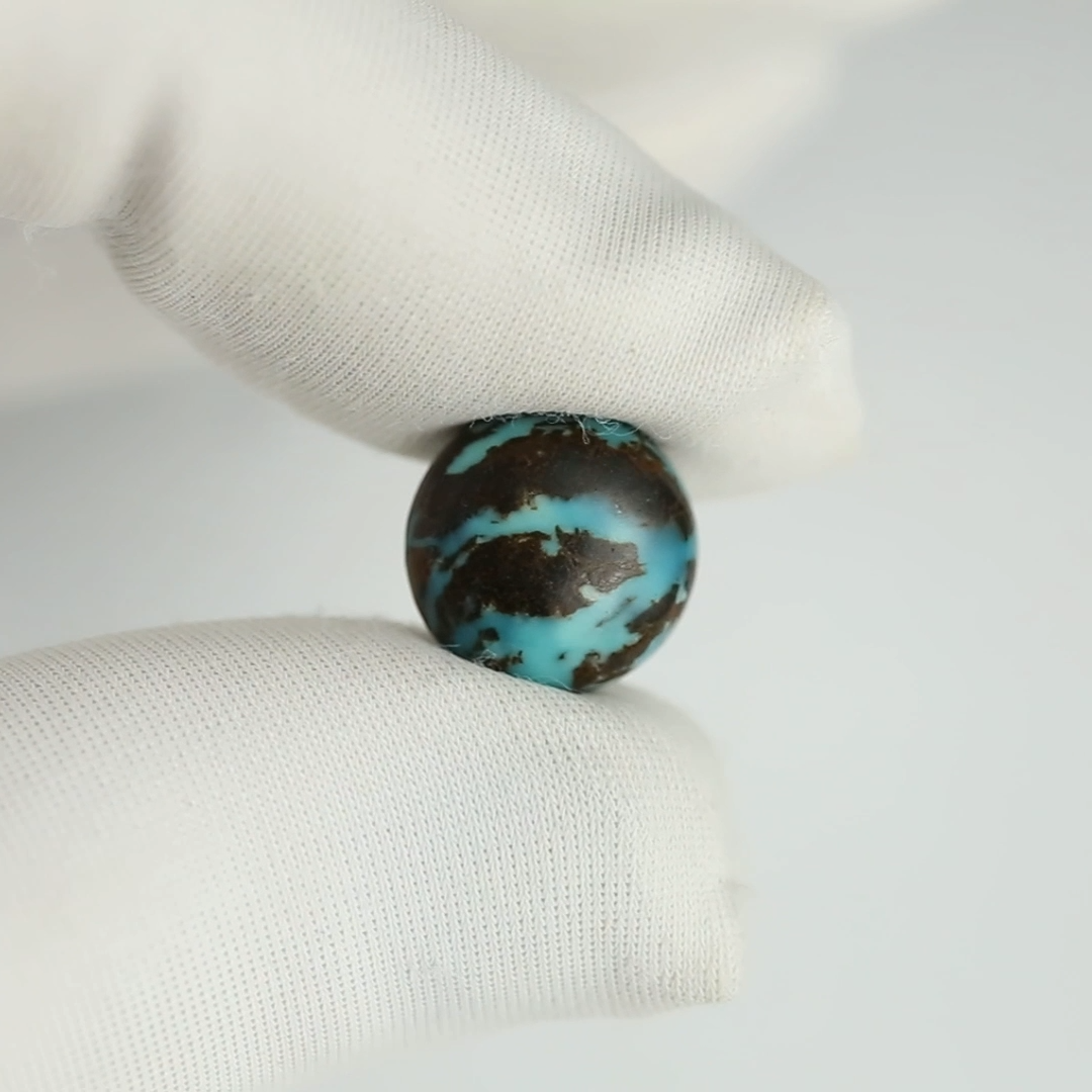 Turquoise stone held between white gloves on a light gray background