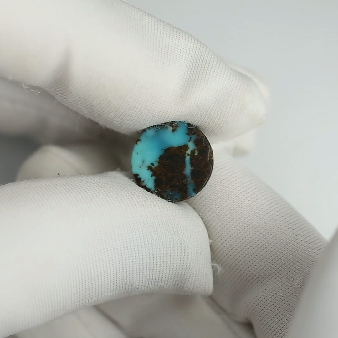 Turquoise stone held between two white gloved fingers on a light gray background